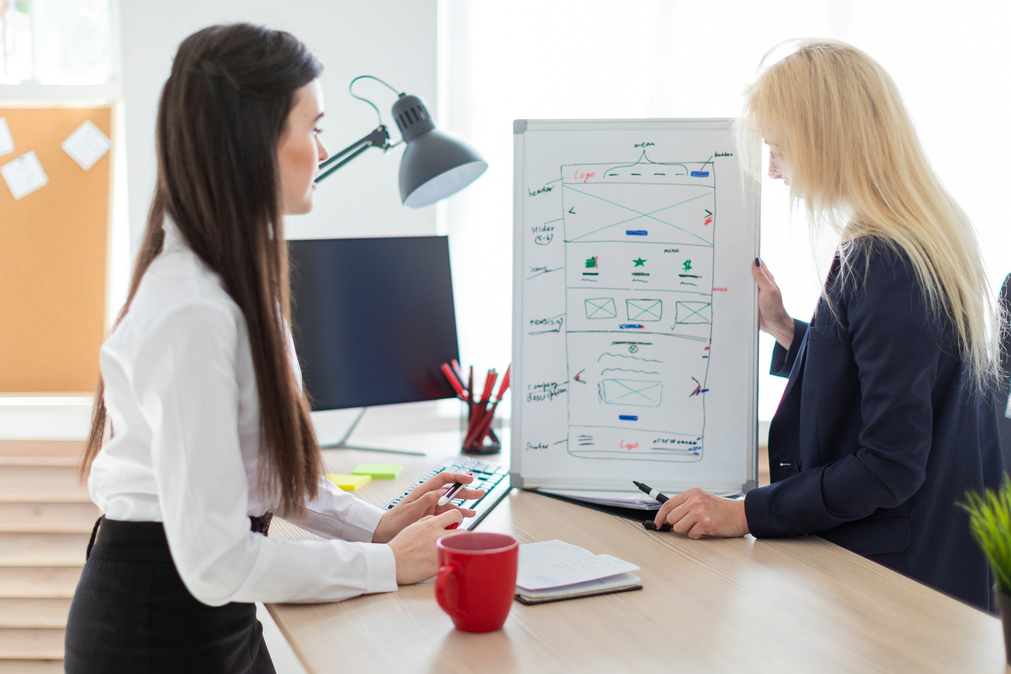 Two girls in the office discussing the project on a magnetic Board.